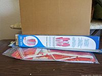 Two packaged sash rods and vintage-style hanging laundry racks laid on wooden surface against cardboard background.