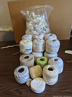 Balls of Perle cotton thread and smaller balls of crochet thread in varying colors arranged on a table with a large plastic bag of sewing trims behind.