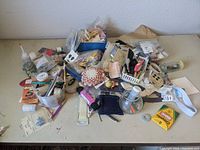 Full view of the sewing notions lot showing multiple small containers and loose items spread out on a table, including threads, pins, scissors, and other sewing tools.