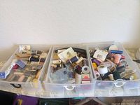 Three plastic storage bins filled with assorted sewing thread spools and sewing notions on a table covered with fabric