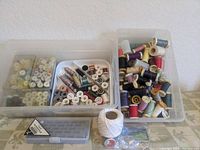 Plastic storage bins filled with multiple spools of vintage sewing thread, showing a variety of colors and materials with some labels visible.