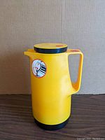 Side view of yellow insulated decanter with handle and lid on top showing the Dr. Zimmermann logo sticker.