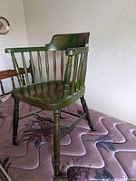 Full view of the vintage green wooden chair showing the spindle back, arms, and turned legs.