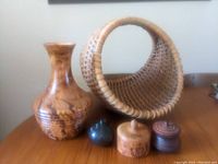Wicker basket, wooden vase, small dark green vase, and two small wooden containers with lids arranged on a wooden surface.