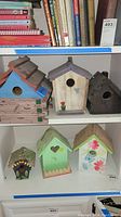 Six bird houses displayed on shelves including largest log cabin style and various painted and natural finishes