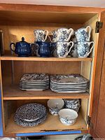 Photo of upper two shelves showing 222 Fifth Adelaide Blue cups, dark blue teapot and sugar pot, and plates and bowls with blue floral design.