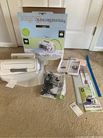 Full lot showing Cricut personal electronic cutter, power adapter in plastic, instruction manuals, and original box on carpeted floor.