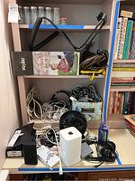 Overview of the electronics lot showing Apple AirPort router, Vornado fan, Mi power bank, charging cords, and other items on a desk shelf.