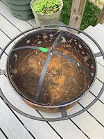 Top view of rusty metal fire pit showing interior and mesh cover with debris.