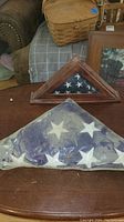 Two veterans folded flags displayed on a table, one in a clear plastic sleeve and the other framed in a wooden case, showing signs of dirt on the covers.