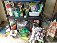 Shelf and floor view showing various garden chemical bottles, bags of peat moss, compost, and sand or stone bags, and a green sprayer