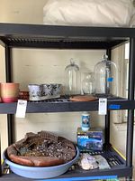 Shelf with planters, glass bell jars, ceramic pots, wood terrarium remnants in blue plastic tray, small aquarium accessory box, and small packages.