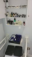 Wide photo showing shelves with multiple essential oil bottles and a carrying case with blue glass bottles on a footstool.