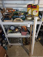 Full shelf view showing assorted paint brushes, tape rolls, caulking gun, door handles, and packaged fire alarms.