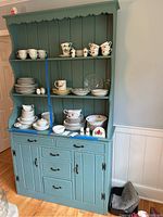 Front view of painted green knotty pine hutch with two open shelves and base cabinets/drawers, displaying various dining items (not included). Scalloped trim detail visible.