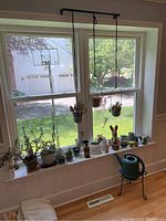 Photo of window ledge with multiple succulent plants in assorted pots, two hanging pots suspended by black cord, and green watering can on floor nearby.