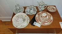 Full overview photo of the collection showing plates, bowls, teapot, teacups and saucers arranged on wood cabinet.