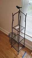Photo of the metal shelving stand showing its full height and design near a window and metal basket beside it.