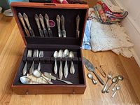 Open wooden case showing knives, forks, spoons in felt-lined upper tray, lower drawer and loose pieces outside.