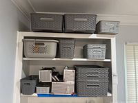 Wide shot of multiple plastic storage bins arranged on a white shelf, including gray and beige bins of various sizes.