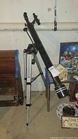 Long black Saturn by Meade telescope on a silver tripod, showing full height in a basement environment alongside other miscellaneous items.