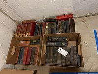 Four boxes of assorted vintage books with visible wear and soiling, showing titles and binding styles.