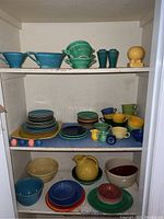 Wide view of shelves filled with stacked colorful ceramic dishes including plates, bowls, cups, and pitchers.