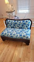 Full front view of vintage mahogany love seat showing curved wooden frame and blue floral upholstery.