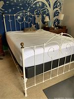 Front side view of the bed frame showing the brass finial on a corner post and the decorative curved metal design on the headboard and footboard.