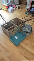 Two vintage wooden dairy crates with metal reinforced corners containing glass jars, wooden tray, metal cane, green plastic tray, metal containers, and metal rack on floor.
