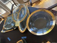 Four clear Annie Glass pieces on dark tabletop near window: large round bowl at front right, deep oval bowl with sticker at back, square platter beneath triangular dish, and triangular three-sectioned dish with gold rim.