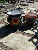 Three ceramic planters displayed on stone patio, includes one large handles planter, one medium orange-rim planter, one small scalloped-edge pot