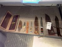 Wide view of seven knives and sheaths on shelf