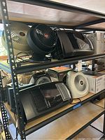 Shelf of fans and space heaters showing multiple units including Lasko and Vornado fans and heaters.