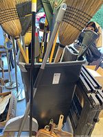 Black plastic bin filled with long-handled brooms and rakes