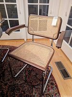 Front view of one armchair showing walnut frame, cane seat and back, and chrome cantilever base