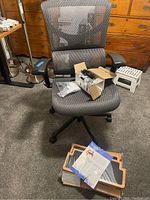 Assembled mesh office chair on caster base with unassembled stool panels and hardware box on seat and floor