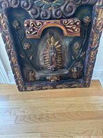 Full view of the wood carving showing central Virgin of Guadalupe figure with floral and leaf motifs framed by scrollwork.