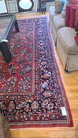 Overall view of rug in living room under coffee table showing red field and navy floral border next to sofa.