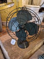 Front view of antique Arctic Aire electric fan showing metal blades and distinctive wire cage with label on base.