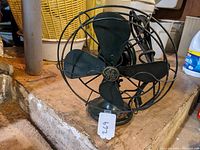 Full view of the vintage 12-inch General Electric fan showing black metal blades and wire protective cage on its base.