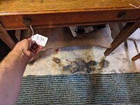 Close-up of front apron showing bead molding, ornate metal drawer pull and partial lower shelf.