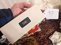 White rectangular box held in hand with black Cross logo on the middle front.