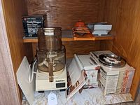 Photo of assembled Cuisinart DLC-10 Plus food processor with the discs, whisk attachment box, smaller chopper box, and mandolin on a shelf.