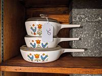 Side view of the stacked three-piece set of CorningWare Country Festival pattern cookware stored on a shelf.