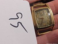 Close-up of Hamilton Art Deco wristwatch showing rectangular gold-tone case, dial with aged patina, gold Arabic numerals, and subsidiary seconds dial.