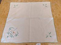 Full view of white square tablecloth showing embroidered design in one corner and shamrocks in the others.