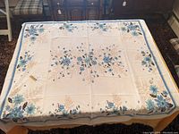 Full view of the linen tablecloth spread on a table showing the blue floral design and scalloped edges.