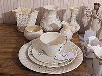 Wide view showing all nine pieces of Belleek porcelain including vases, plates, and cups with shamrock details on wooden surface