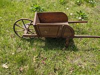 Side view of vintage wooden wheelbarrow showing single spoked wheel, removable sides and long handles on grass